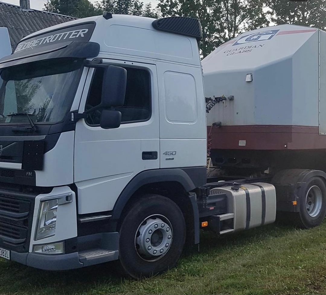 Biała ciężarówka Volvo FM 450 z naczepą Guardian Glass na trawiastym terenie.