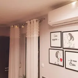 Biały klimatyzator ścienny w nowoczesnym salonie z dekoracjami ściennymi i zasłonami.