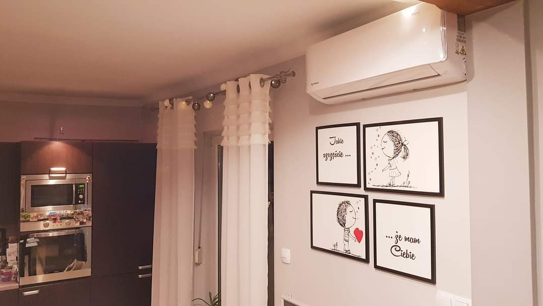 Biały klimatyzator ścienny w nowoczesnym salonie z dekoracjami ściennymi i zasłonami.