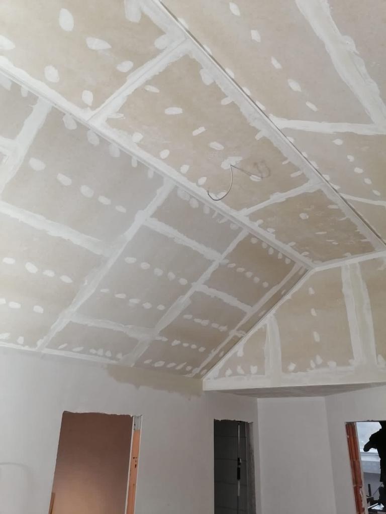 Sufit podwieszany z płyt gipsowo-kartonowych, szpachlowane łączenia i widoczne wkręty, surowy stan przed malowaniem, widoczne fragmenty ścian i ościeżnic drzwiowych.