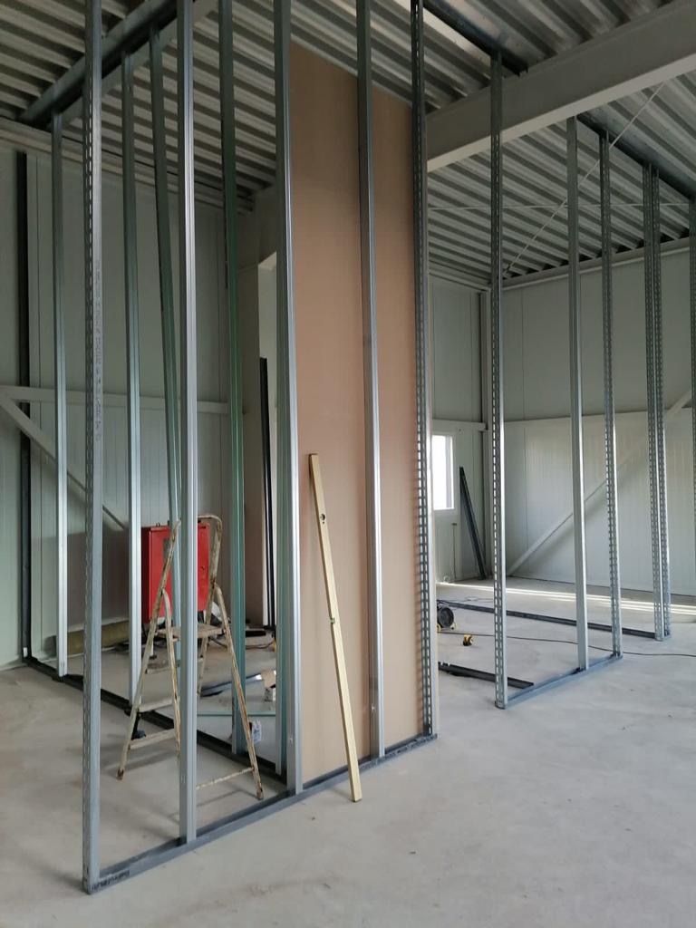 Wnętrze w trakcie montażu ścian działowych z płyt kartonowo-gipsowych na metalowej konstrukcji, widoczna poziomica oparta o płytę, drabina i narzędzia w tle.