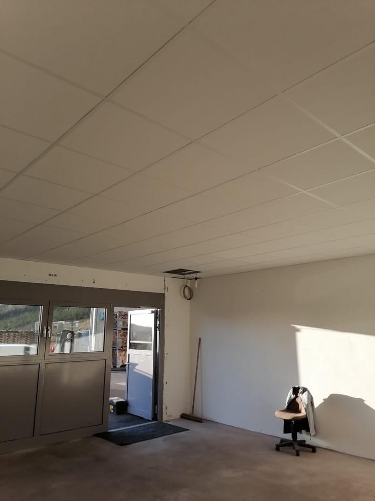 Wnętrze biura przed malowaniem: widoczne panele sufitowe, ściany przygotowane do malowania, biurowe krzesło i drzwi wejściowe.
