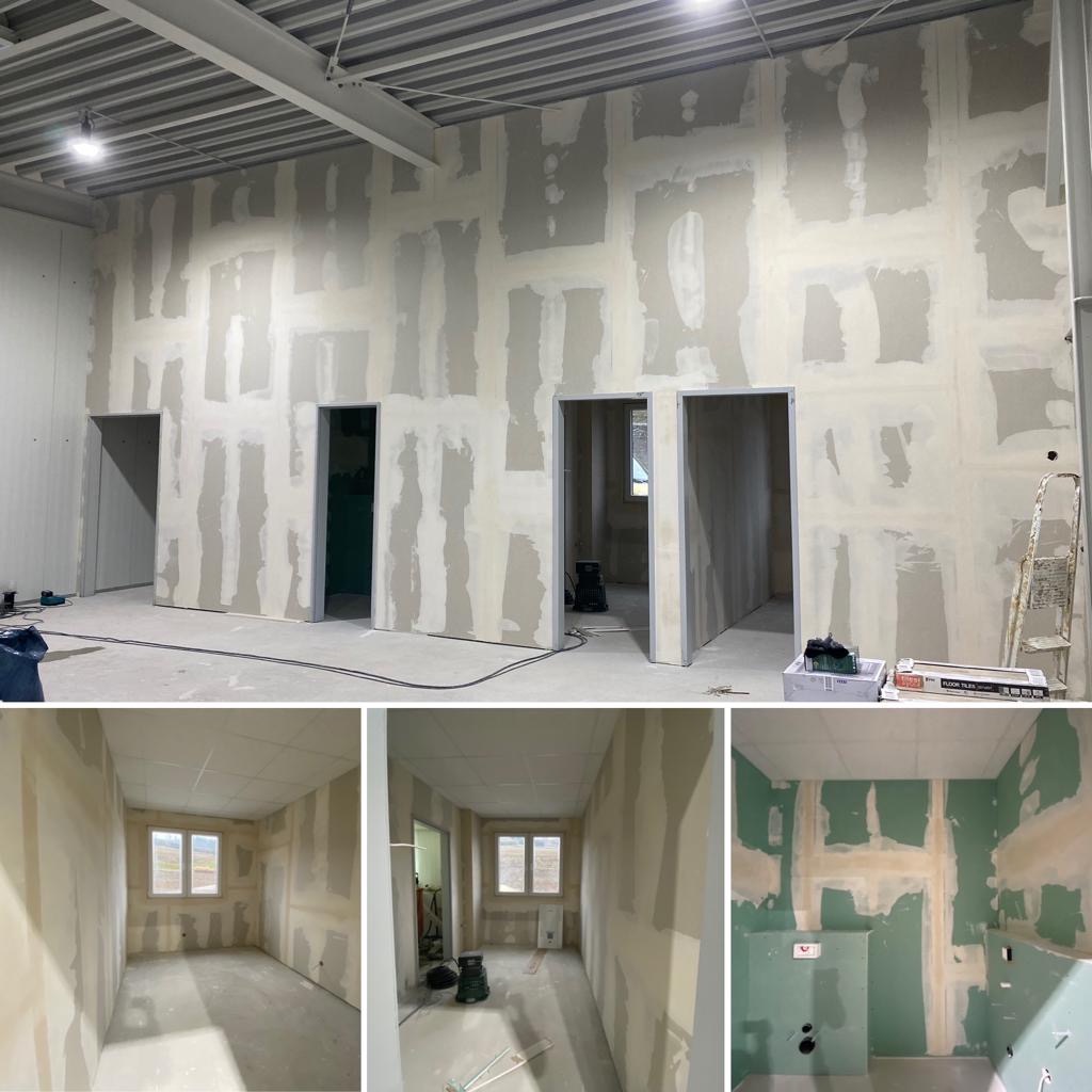 Wnętrze w trakcie prac wykończeniowych: ściany pokryte płytami gipsowo-kartonowymi, z widocznymi łączeniami szpachlowanymi, przygotowane do dalszych etapów prac w dużym pomieszczeniu z kilkoma...