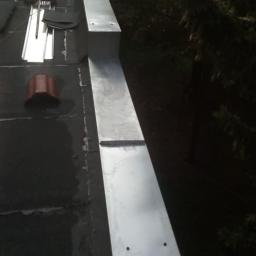 volidarek - Świeżo zamontowana, długa, metalowa obróbka blacharska na krawędzi płaskiego dachu pokrytego papą; widoczne narzędzia i elementy dekarskie.