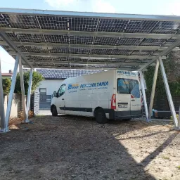 Zadaszenie fotowoltaiczne w Częstochowie nad miejscem parkingowym, pod którym stoi biały samochód dostawczy z logo firmy instalującej panele.