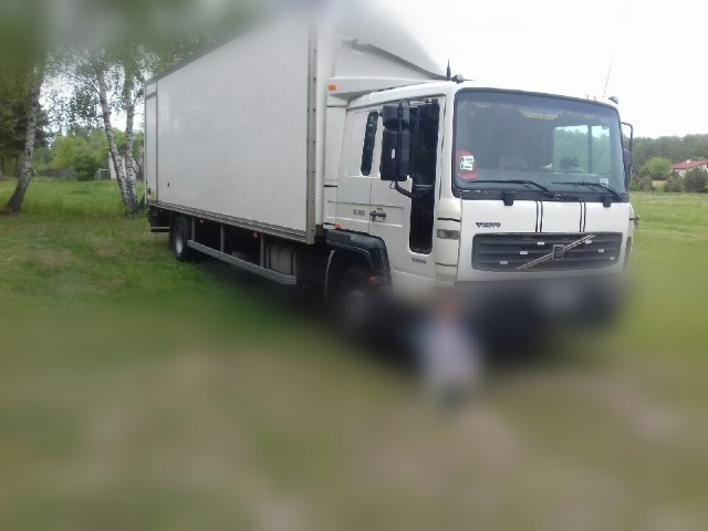 Biała ciężarówka Volvo FL6 z zabudową skrzyniową na trawiastym terenie, z widocznymi trzema czarnymi pasami na grillu i anteną na dachu kabiny.