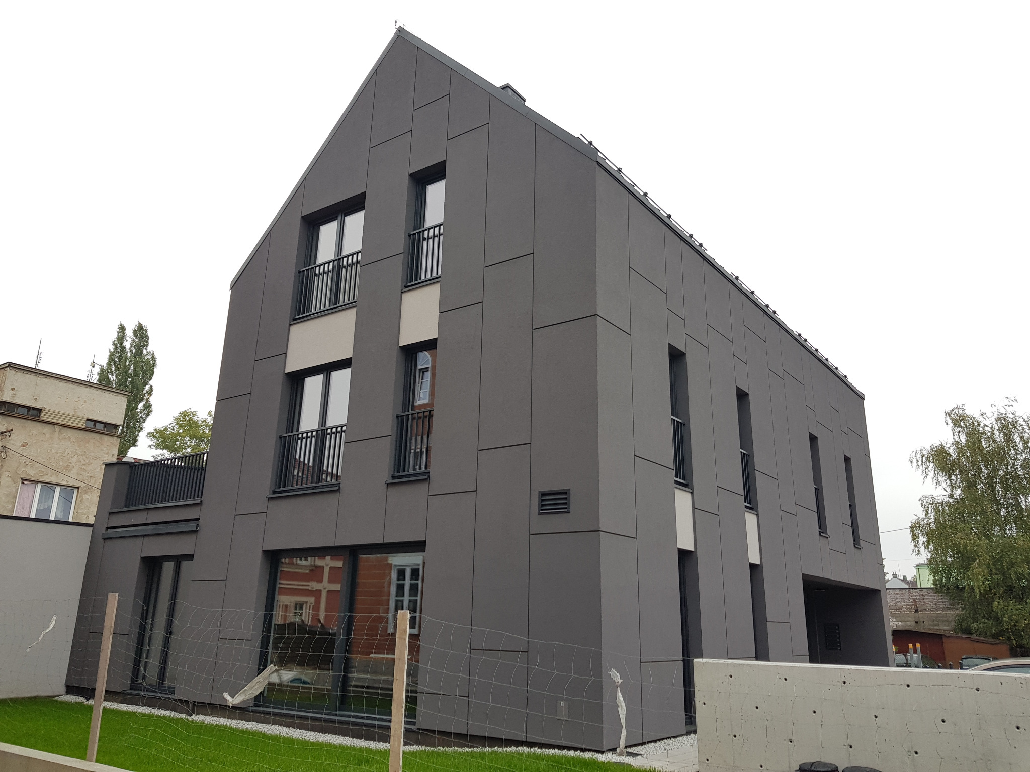 Nowoczesny dom jednorodzinny z szarą elewacją w panelach, widok z dołu, ogrodzenie siatkowe w pierwszym planie.