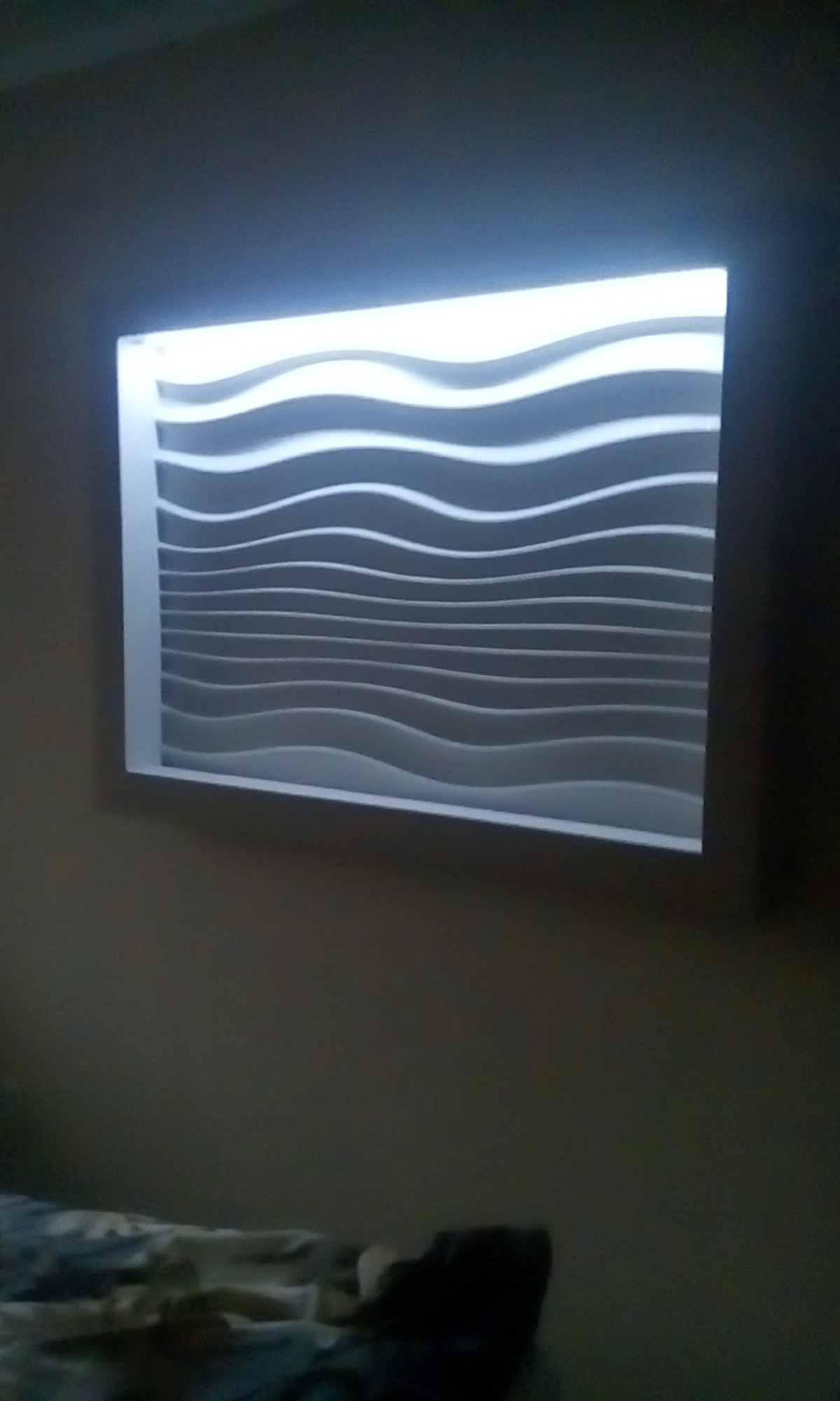 Panel dekoracyjny 3D z falistymi liniami, podświetlony, zamontowany na ścianie w pokoju. Słabe oświetlenie otoczenia.