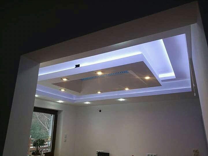 Wielopoziomowy sufit podwieszany z oświetleniem LED w chłodnych barwach, widok z dołu na wykończone wnętrze pokoju z oknem.