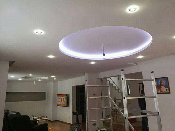 Salon z białym sufitem podwieszanym z okrągłym, podświetlanym elementem centralnym oraz dodatkowymi punktami świetlnymi, widoczna drabina malarska.