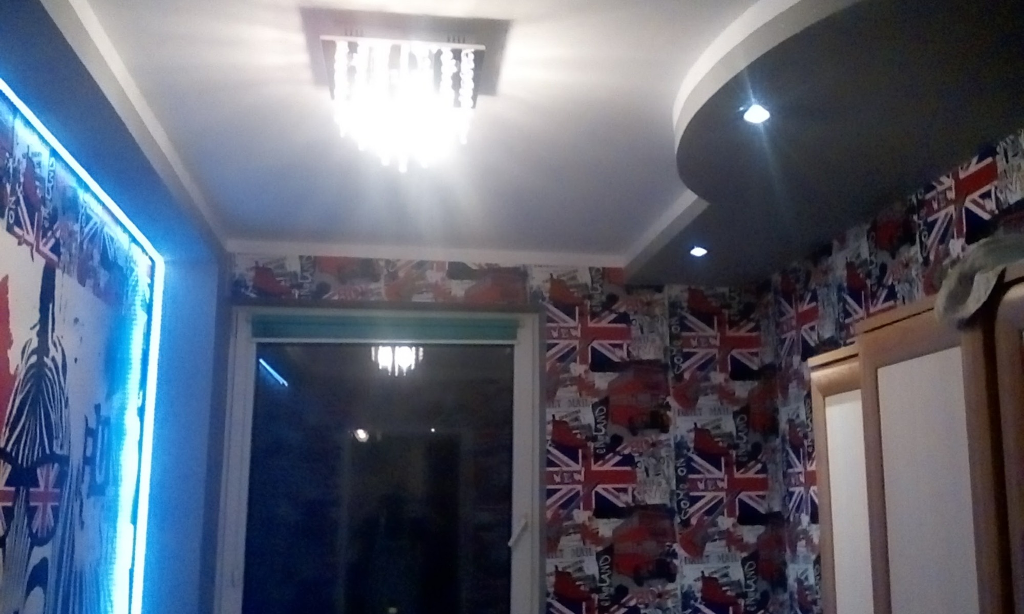 Pokój z tapetą w motywy brytyjskie, oświetlony neonowym światłem LED i kryształowym żyrandolem, z podwieszanym sufitem z punktowymi lampami.