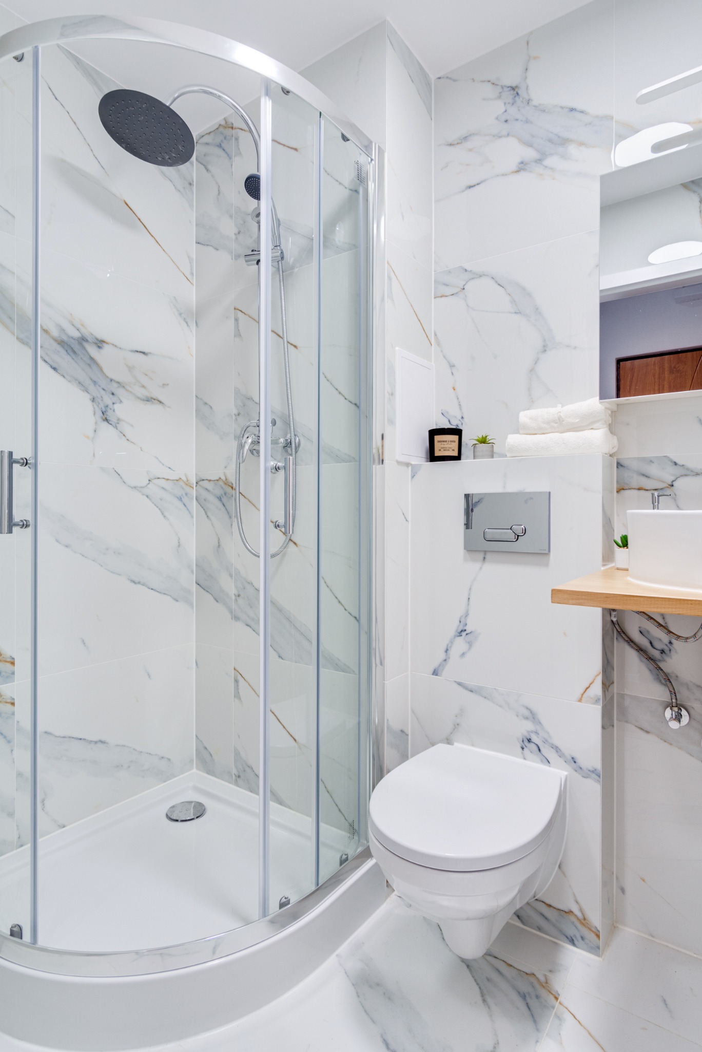 Nowoczesna łazienka z kabiną prysznicową typu walk-in, białą ceramiką i marmurowymi płytkami ściennymi z delikatnymi złotymi żyłkami.