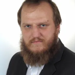 Portret mężczyzny z brodą w garniturze na białym tle, patrzącego wprost.