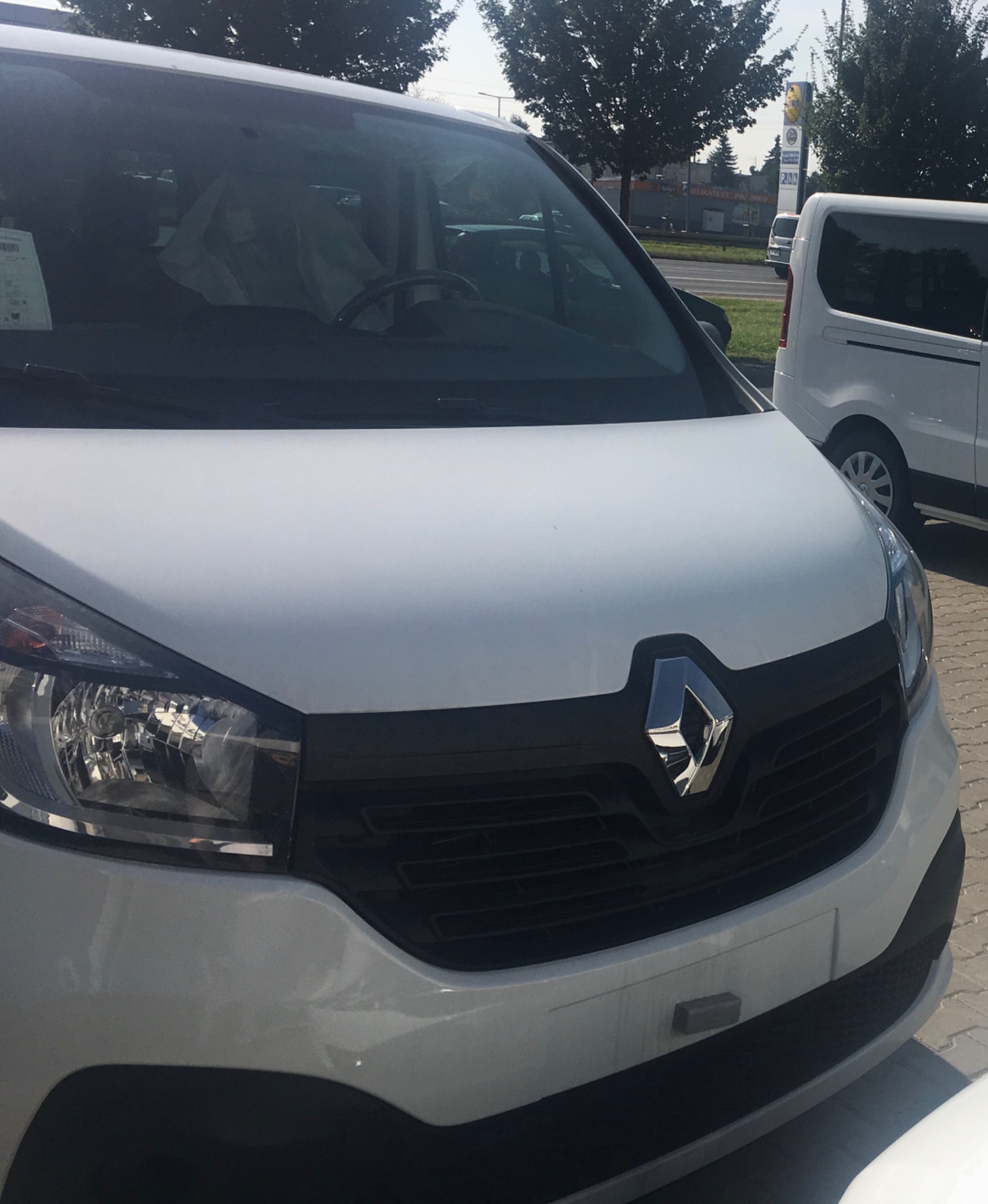 Biały samochód dostawczy Renault z widocznym logo na tle miejskiego krajobrazu i innych pojazdów.