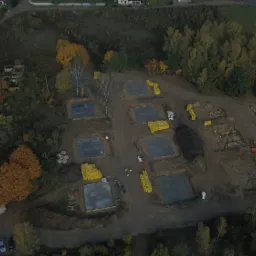 Widok z lotu ptaka na plac budowy w Olsztynie z wykopanymi fundamentami pod kilka domów, częściowo już wylane płyty fundamentowe, obok żółte bloczki i pracownicy w kamizelkach.