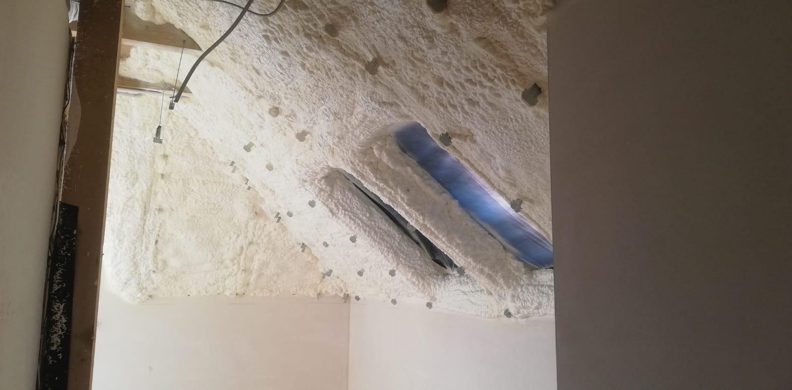 Poddasze ocieplone pianką poliuretanową, widoczne okna dachowe z obrzeżami pokrytymi pianką, liczne metalowe kołki mocujące w pianie.