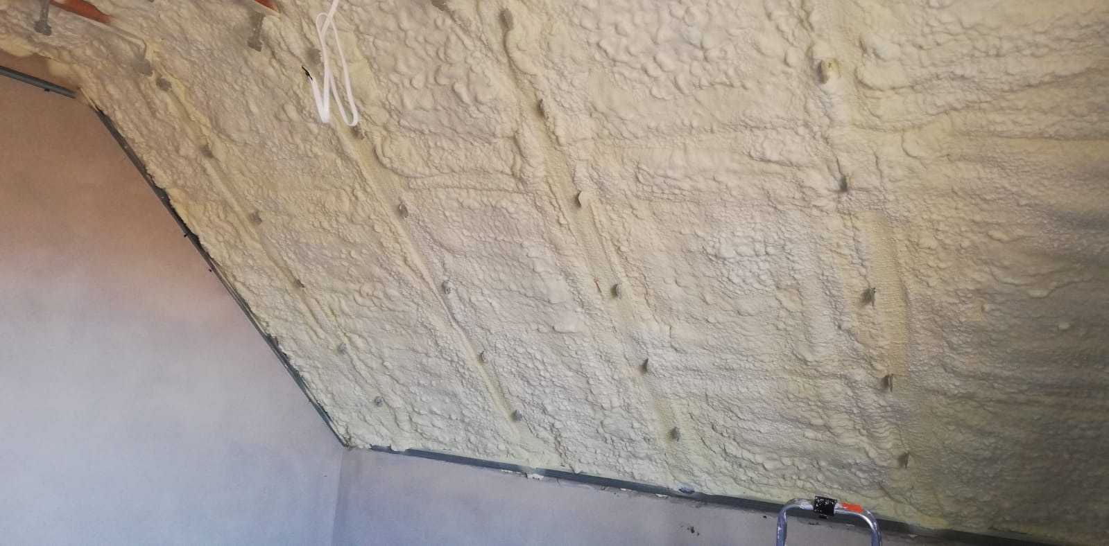 Poddasze ocieplone pianką poliuretanową, widoczne metalowe profile konstrukcyjne i wystające kołki montażowe, białe przewody elektryczne zwisają z sufitu.