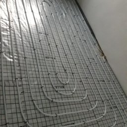 Usługi Hydrauliczne Łukasz Lewandowski - Białe rury systemu rozprowadzenia ciepła ułożone na siatce z tworzywa, przygotowane do zalania w posadzce.