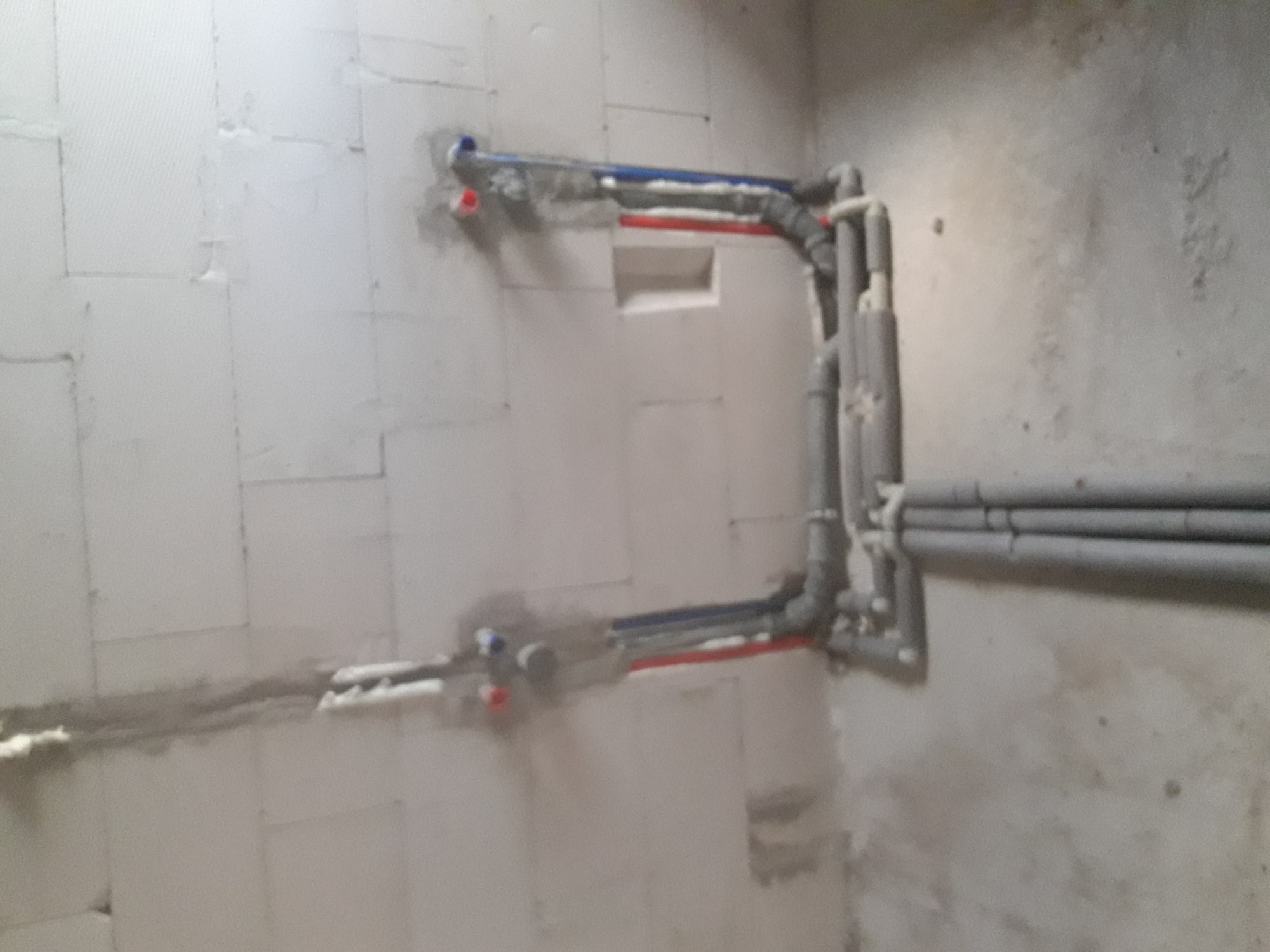 Świeżo zamontowane, izolowane rury wodne i grzewcze w surowym pomieszczeniu z bloków, z widocznymi nieotynkowanymi ścianami.