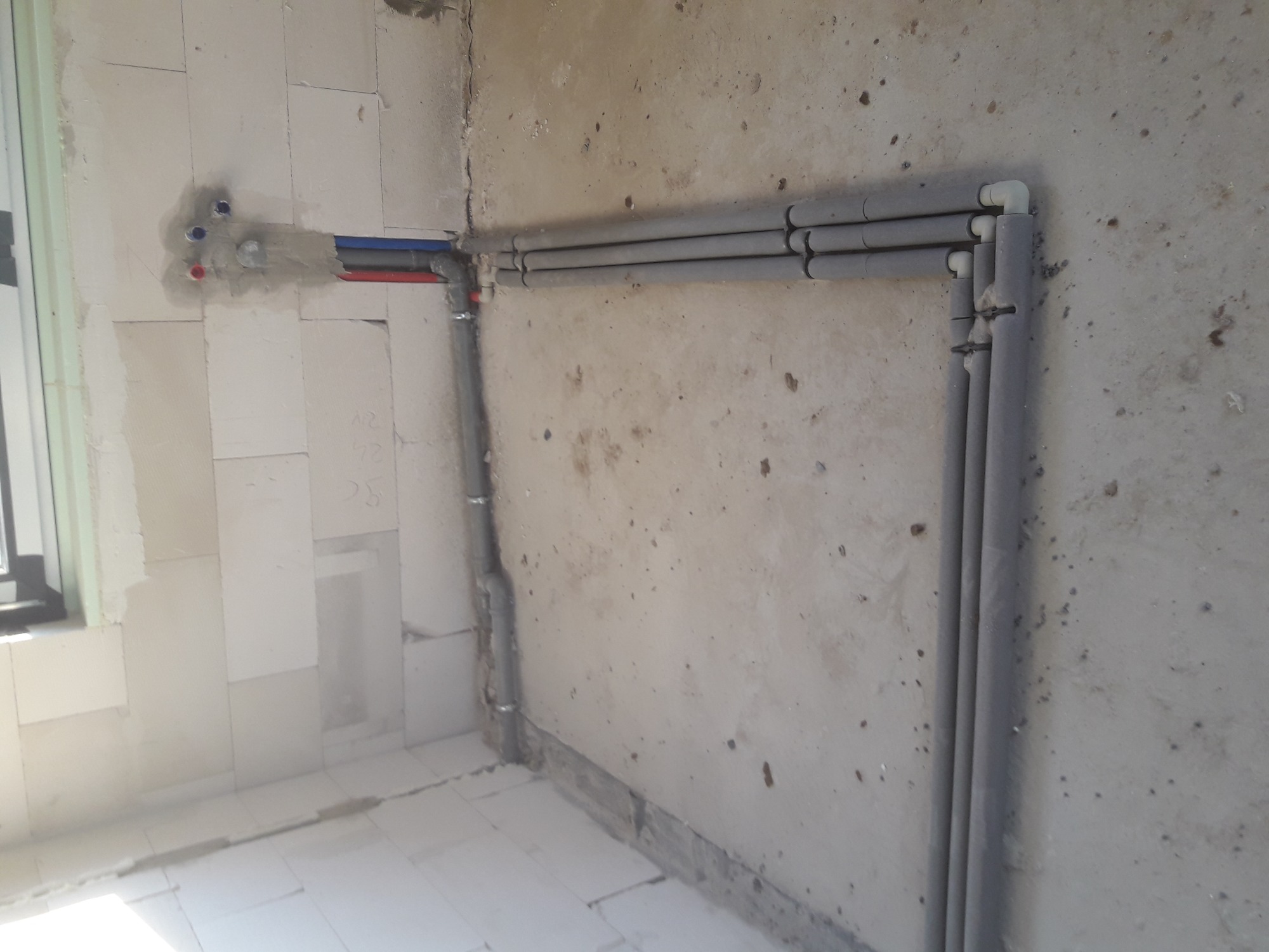 Wewnętrzna instalacja wodna i grzewcza w surowym stanie, rury prowadzone wzdłuż ściany z betonu komórkowego, zabezpieczone izolacją termiczną, widoczne fragmenty instalacji podtynkowych z rurami...