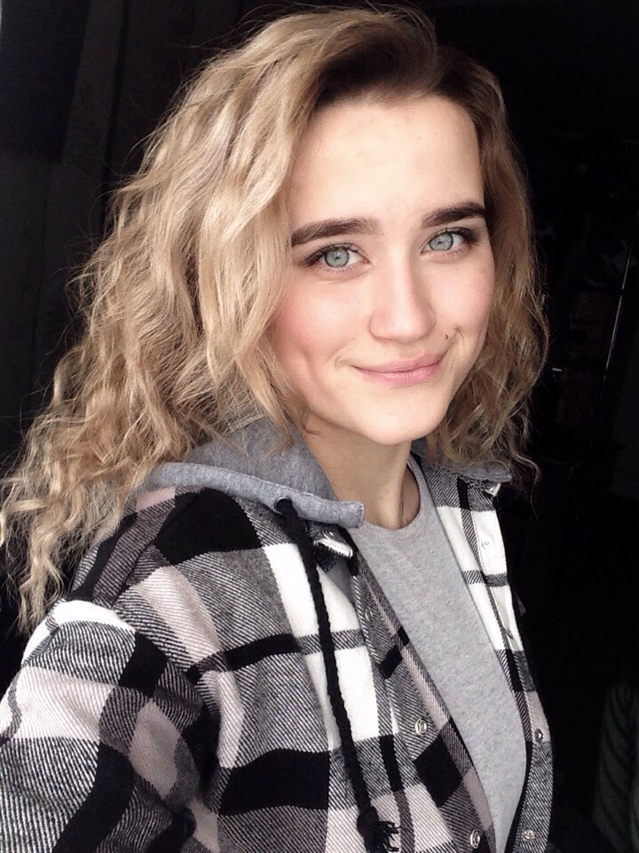 Portret uśmiechniętej kobiety z blond lokami i niebieskimi oczami w czarno-białej flanelowej koszuli z kapturem.