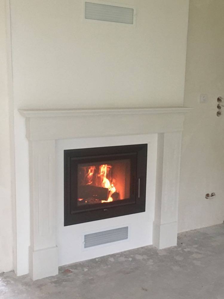 Wnętrze z wkładem kominkowym w obudowie w stylu klasycznym, widoczne płomienie i drewno w palenisku, ściana w trakcie wykończenia.