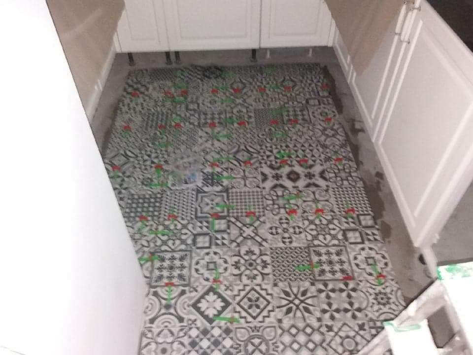 Wzorzysta, czarno-biała podłoga z motywami geometrycznymi i kwiatowymi ułożona w kuchni, widoczne białe szafki kuchenne, etap prac wykończeniowych.