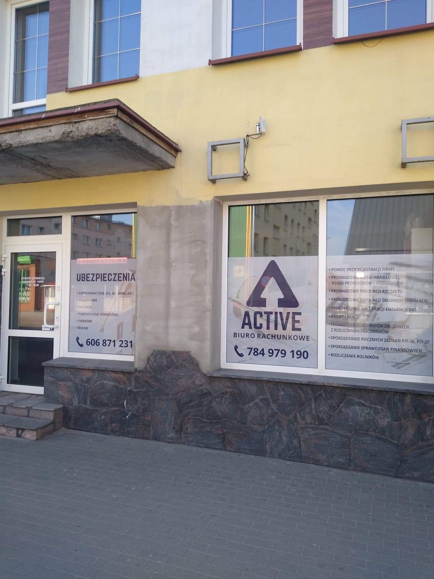 Fasada budynku z dwoma witrynami: po lewej ogłoszenie 'Ubezpieczenia', po prawej 'Active Biuro Rachunkowe' z numerami telefonów.