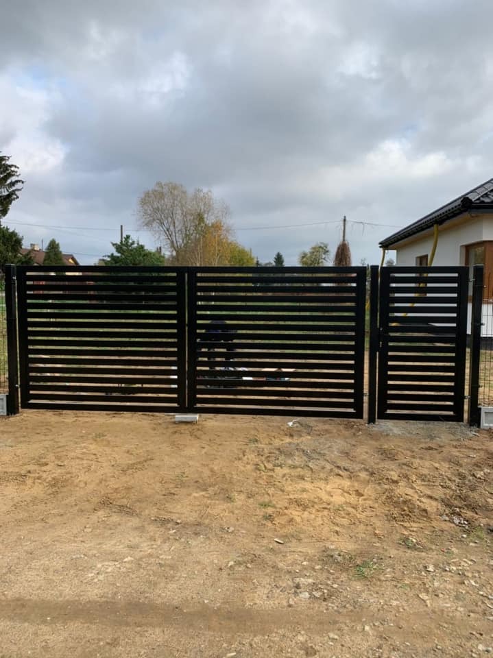 Nowoczesna, pozioma brama panelowa w kolorze czarnym, zamontowana na posesji z widocznym domem w tle i ziemistym podłożem.