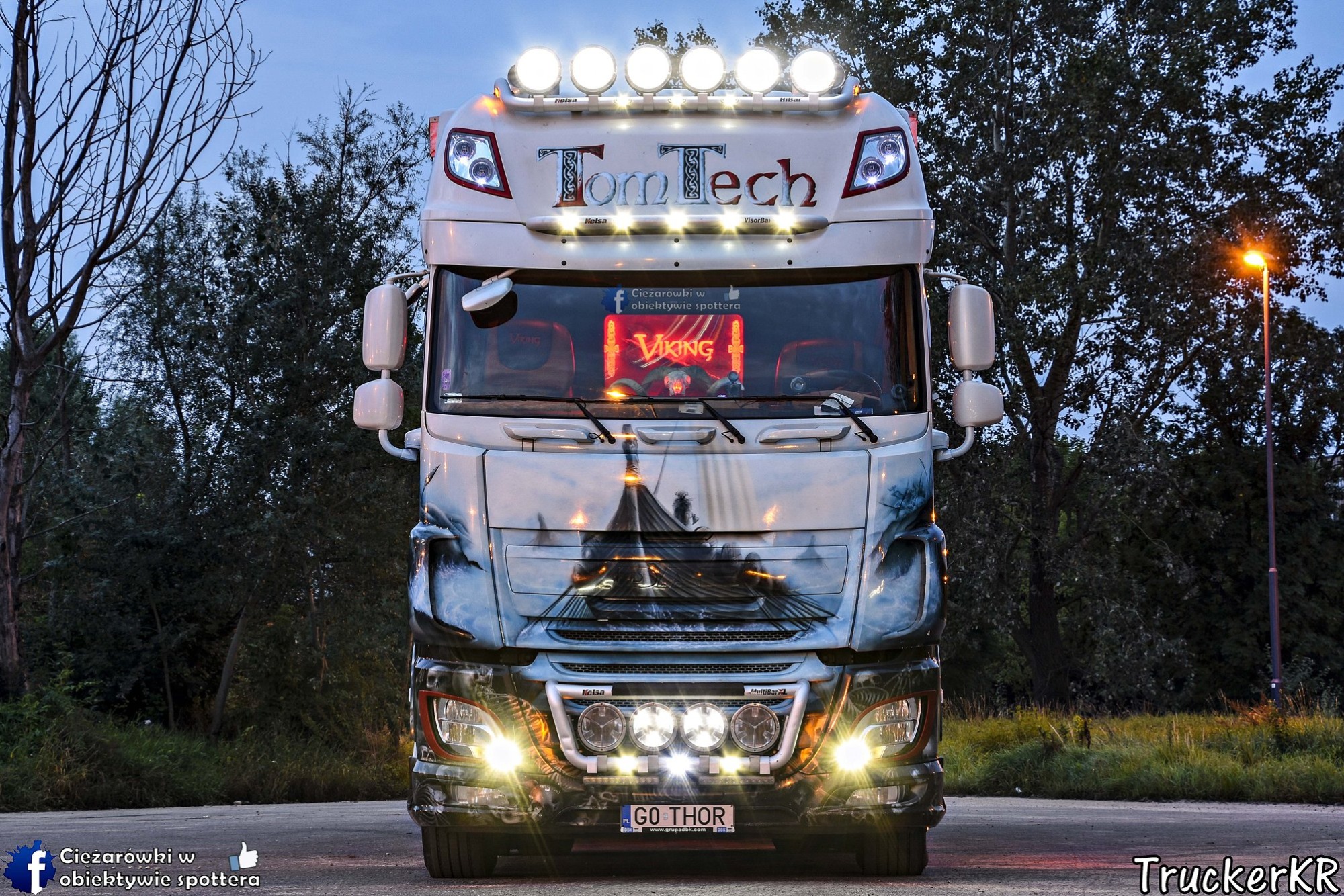 Przód ciężarówki marki TomTech z motywem wikinga na masce, dodatkowym oświetleniem i tablicą rejestracyjną 'GO THOR', sfotografowany z przodu na tle drzew.
