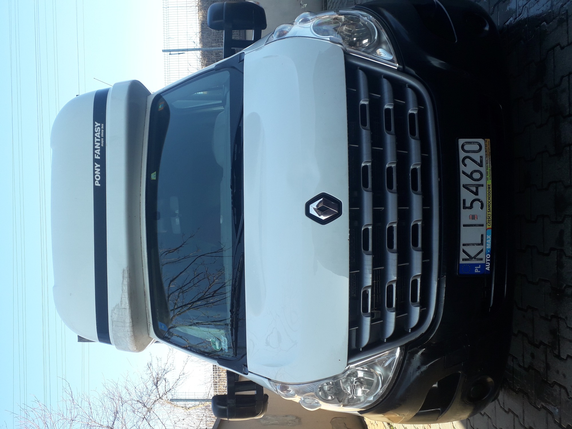 Przód białego samochodu dostawczego marki Renault z nadbudówką 'PONY FANTASY' na dachu, widoczne tablice rejestracyjne KLI 54620.