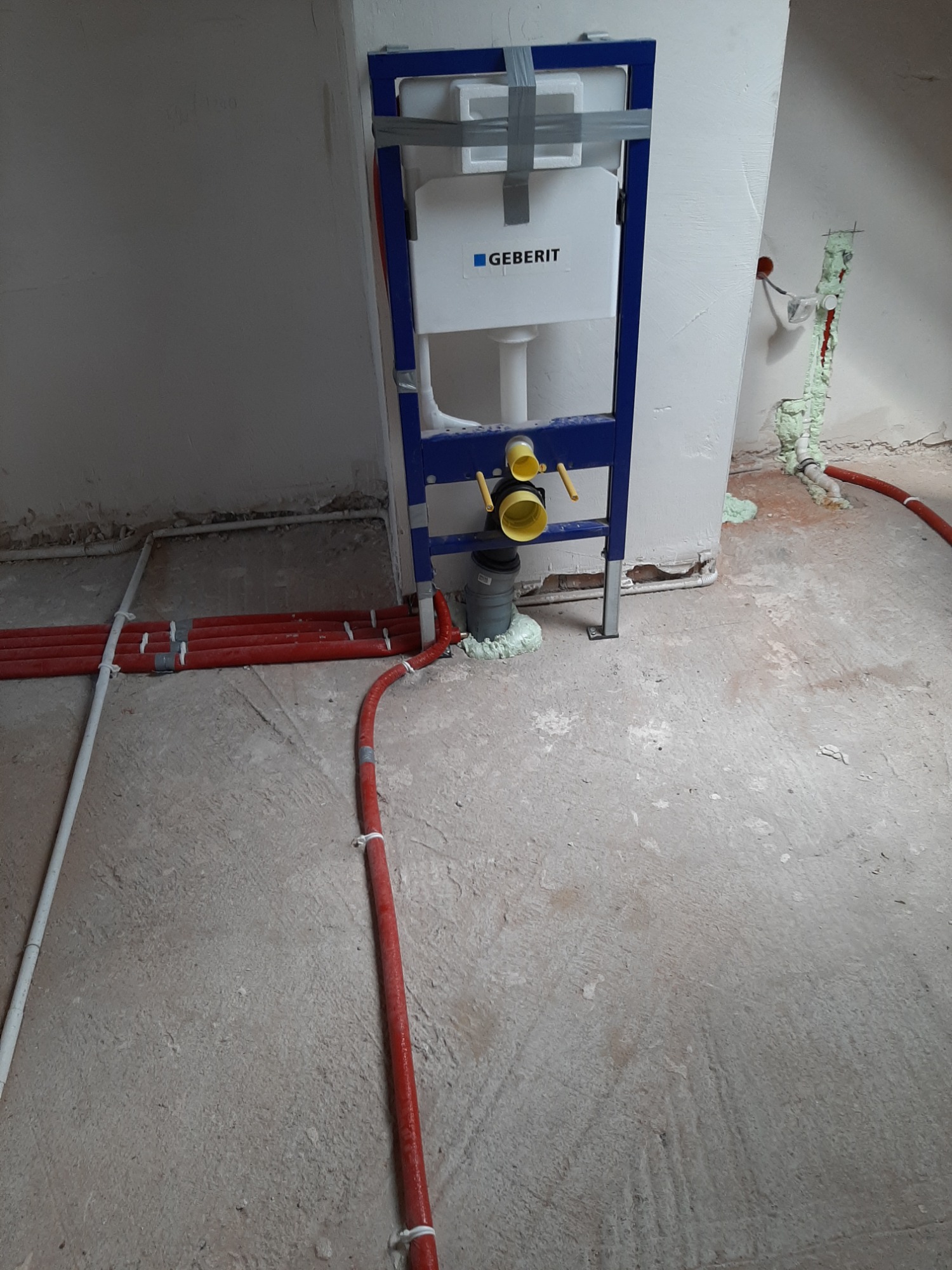 Stelaż podtynkowy Geberit zamontowany na surowym podłożu, widoczne rury instalacji wodnej i kanalizacyjnej zabezpieczone pianką montażową.