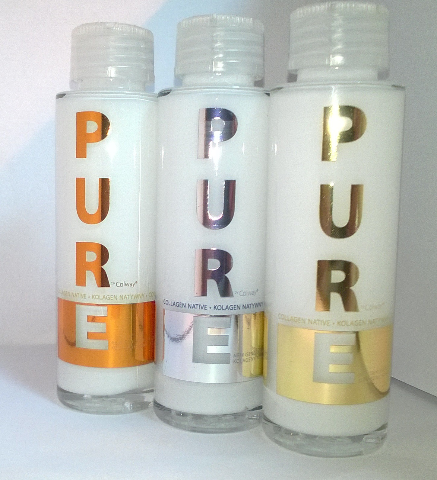 Trzy białe butelki z kolagenem natywnym marki Colway, każda z napisem 'PURE' w innym kolorze: pomarańczowym, srebrnym i złotym, stojące na jasnym tle.