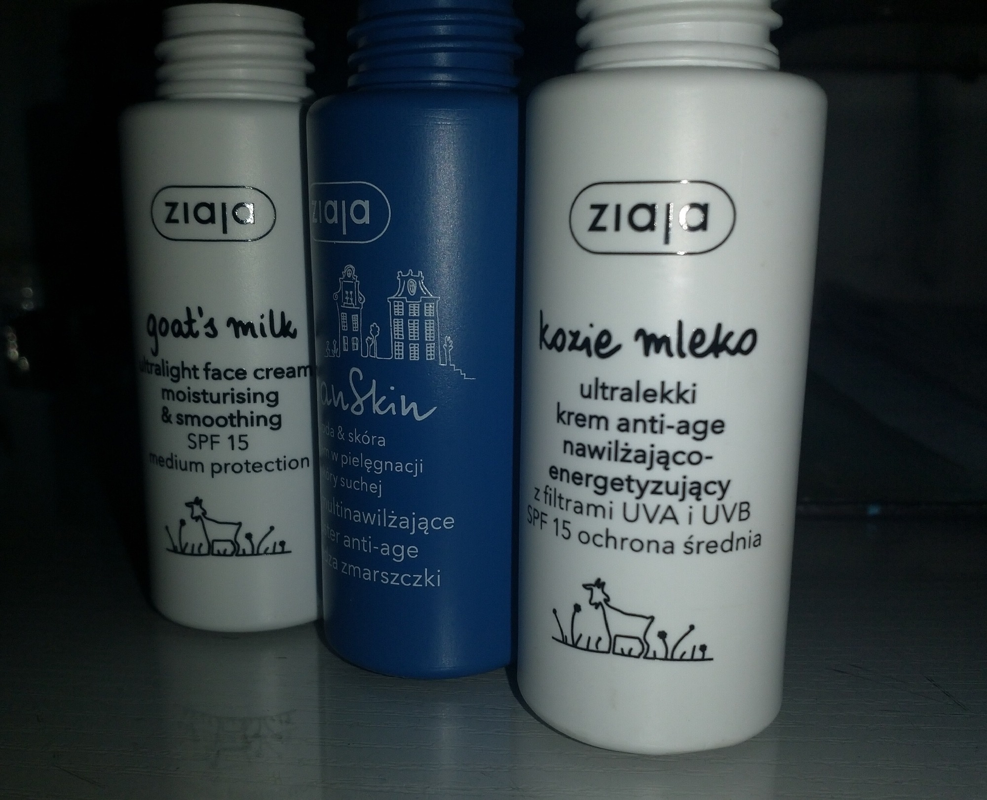 Trzy butelki kosmetyków marki Ziaja, w tym krem do twarzy z kozim mlekiem i krem nawilżający, ustawione obok siebie na ciemnym tle.