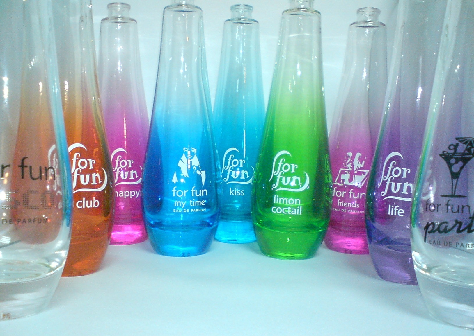 Kolekcja kolorowych, gradientowych flakonów perfum 'for fun' z różnymi nadrukami nazw i grafik, ustawionych obok siebie na białym tle.