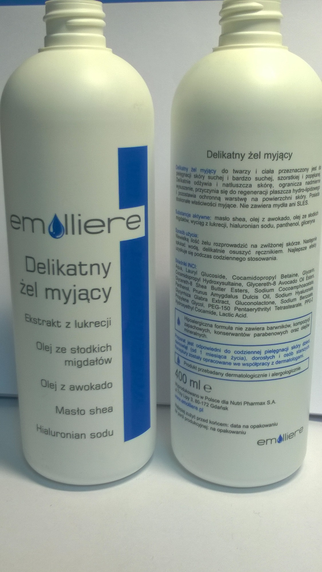 Dwie białe butelki żelu myjącego Emolliere z ekstraktem z lukrecji, olejem ze słodkich migdałów, olejem z awokado, masłem shea i hialuronianem sodu, z widocznymi składnikami i informacjami...