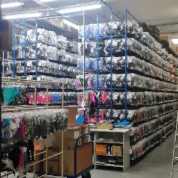 Pełen regałów magazyn z zapakowaną bielizną i odzieżą, wózki transportowe z kartonami na pierwszym planie, oświetlenie przemysłowe.