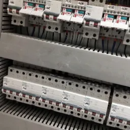 Rozdzielnica elektryczna z bezpiecznikami Siemens i Relpol, widoczne okablowanie i schematy elektryczne na dole kadru.