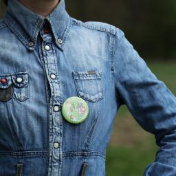 Buttonfly - Osoba w dżinsowej koszuli z przypinką z motywem rycerza i napisem POLSKA na tle zieleni.