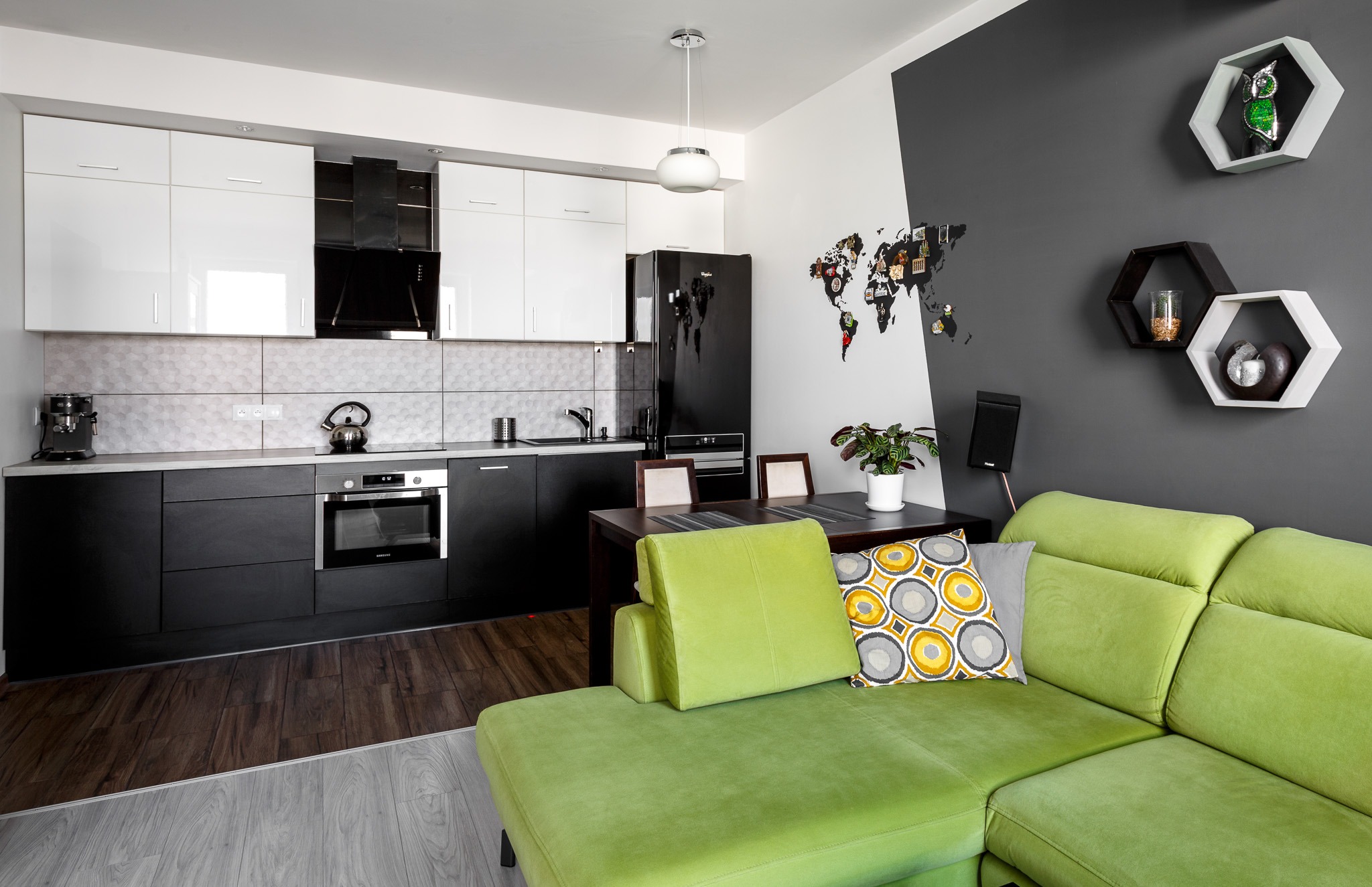Wnętrze nowoczesnej kuchni z salonem, dominują czerń i biel, akcentuje zielona sofa i mapa świata na ścianie.