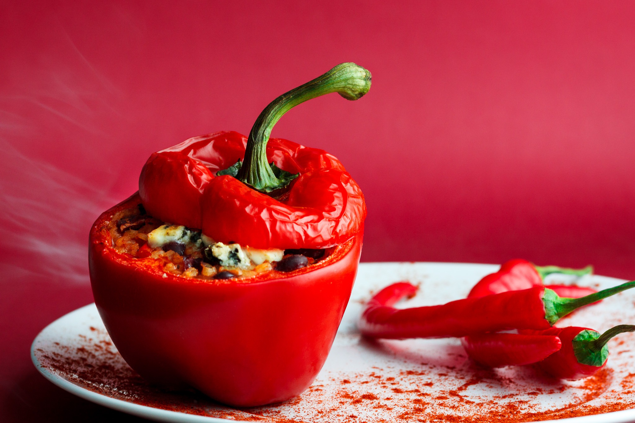 Czerwona papryka faszerowana na białym talerzu z papryczkami chili i przyprawą, na czerwonym tle.