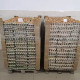 Dwa palety z ułożonymi wytłaczankami z brązowymi jajami, owinięte folią stretch, widoczne w magazynie.