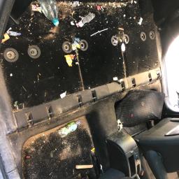 Car wash garage - Bardzo zabrudzone wnętrze samochodu, widoczne śmieci, resztki jedzenia i butelki na podłodze, przed praniem tapicerki.