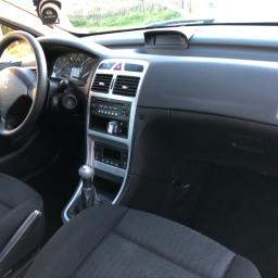 Car wash garage - Wnętrze samochodu Peugeot 307 z widocznymi czarnymi fotelami, deską rozdzielczą z srebrnymi elementami i kierownicą z logo marki.