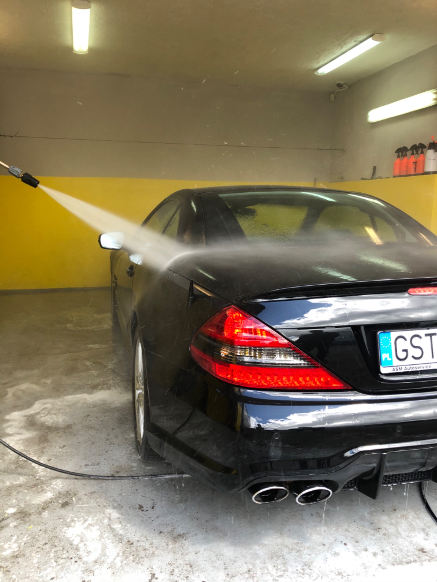 Czarny Mercedes SL podczas mycia ciśnieniowego w myjni, widoczne krople wody na karoserii i tablica rejestracyjna z napisem ASM Autoservice.