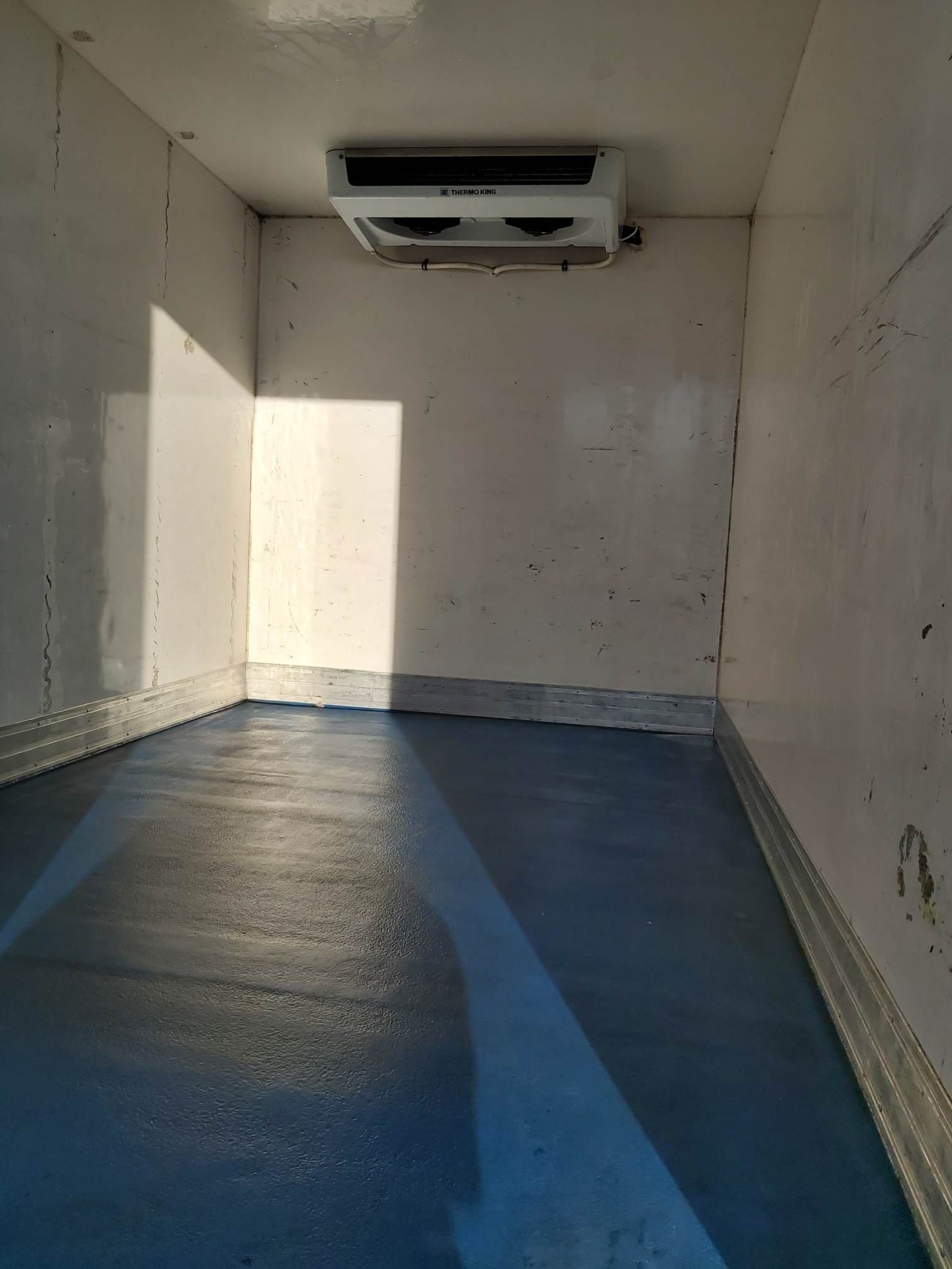 Wnętrze chłodni samochodowej z niebieską podłogą i białą ścianą, widoczny agregat chłodniczy marki Thermo King zamontowany pod sufitem.