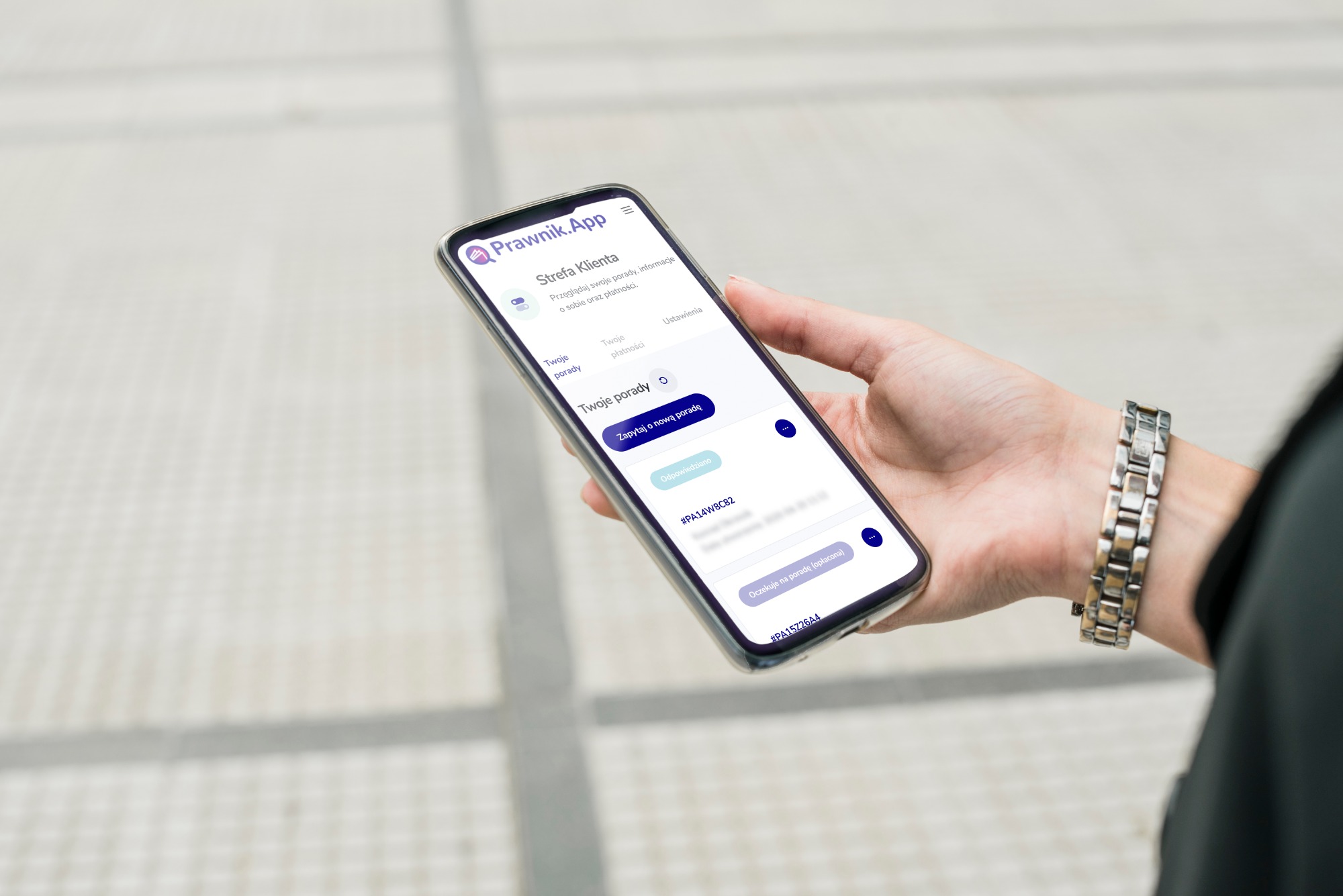 Kobieta trzyma smartfon z otwartą aplikacją Prawnik.App, wyświetlającą strefę klienta z poradami i informacjami o płatnościach. Widoczny jest fragment srebrnego zegarka na nadgarstku.