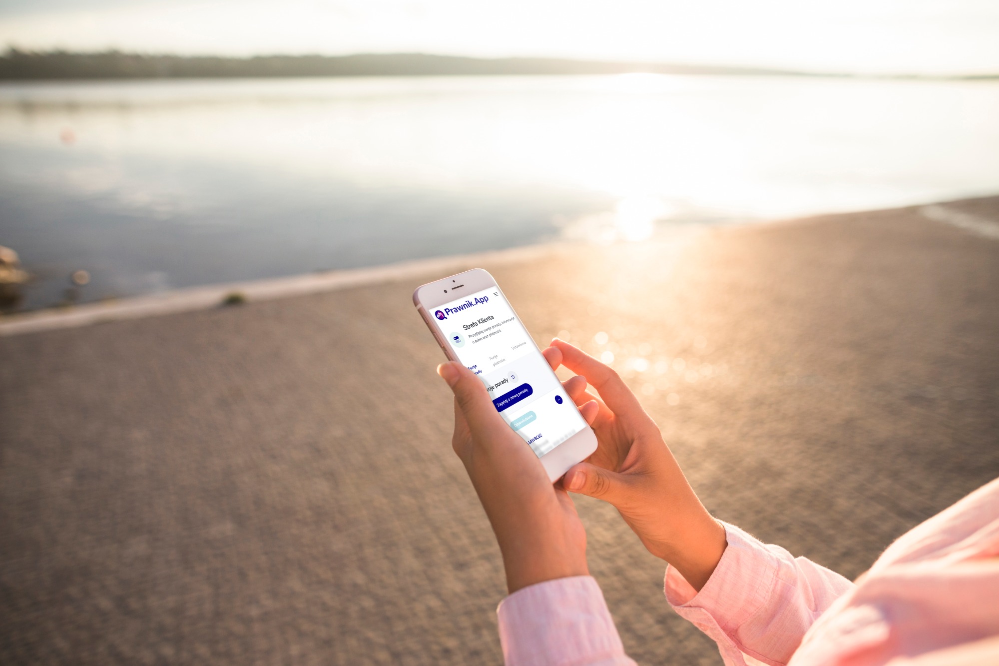 Osoba trzyma smartfon z aplikacją prawną 'Prawnik.App' na tle jeziora w słoneczny dzień, widoczny interfejs klienta z opcjami porad prawnych i płatności.