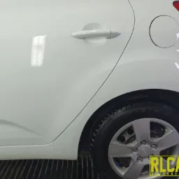 Biały samochód Kia po umyciu, widoczna kropla wody na lakierze, koło z oponą na metalowej kratce, logo firmy autokosmetycznej w prawym dolnym rogu.