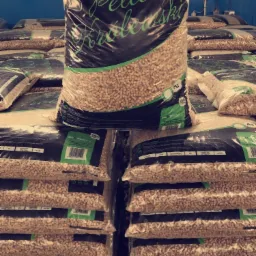 Stos palet z pelletem drzewnym 'Pellet Kr&oacute;lewski' 15 kg, widoczny napis 6 mm, ułożonych rzędami w magazynie.